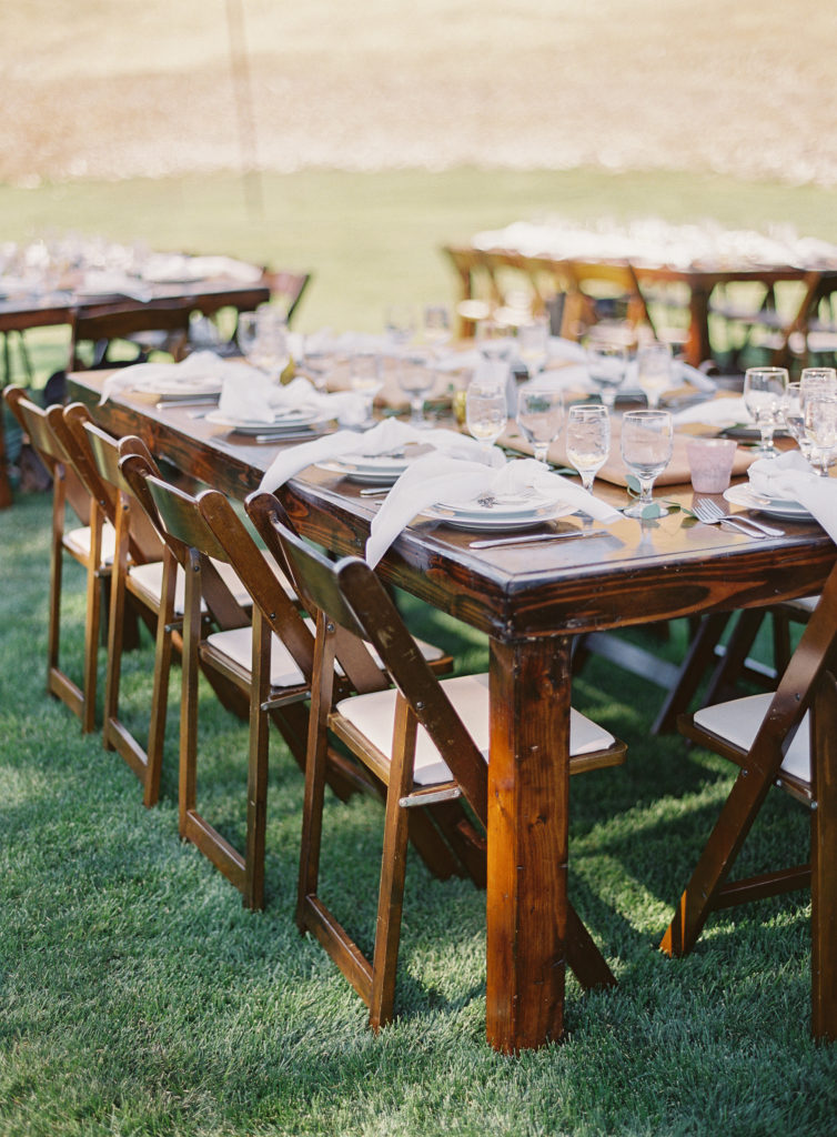 Wedding reception with white napkins tied in a knot on white plates on a farm table