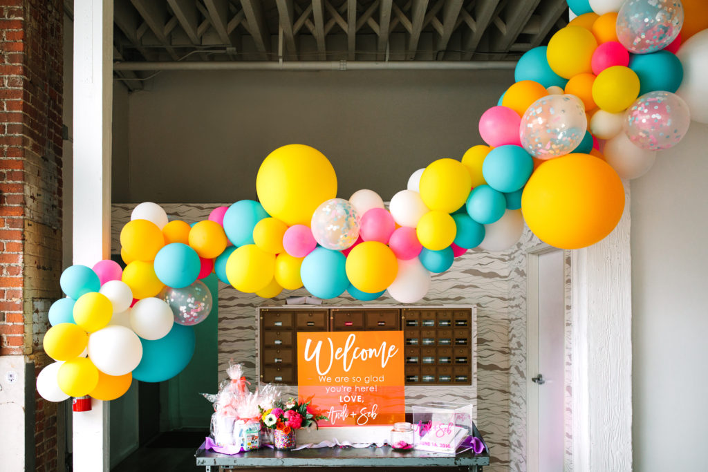 A colorful wedding at Unique Space LA, welcome table with bright acrylic sign and balloon garland