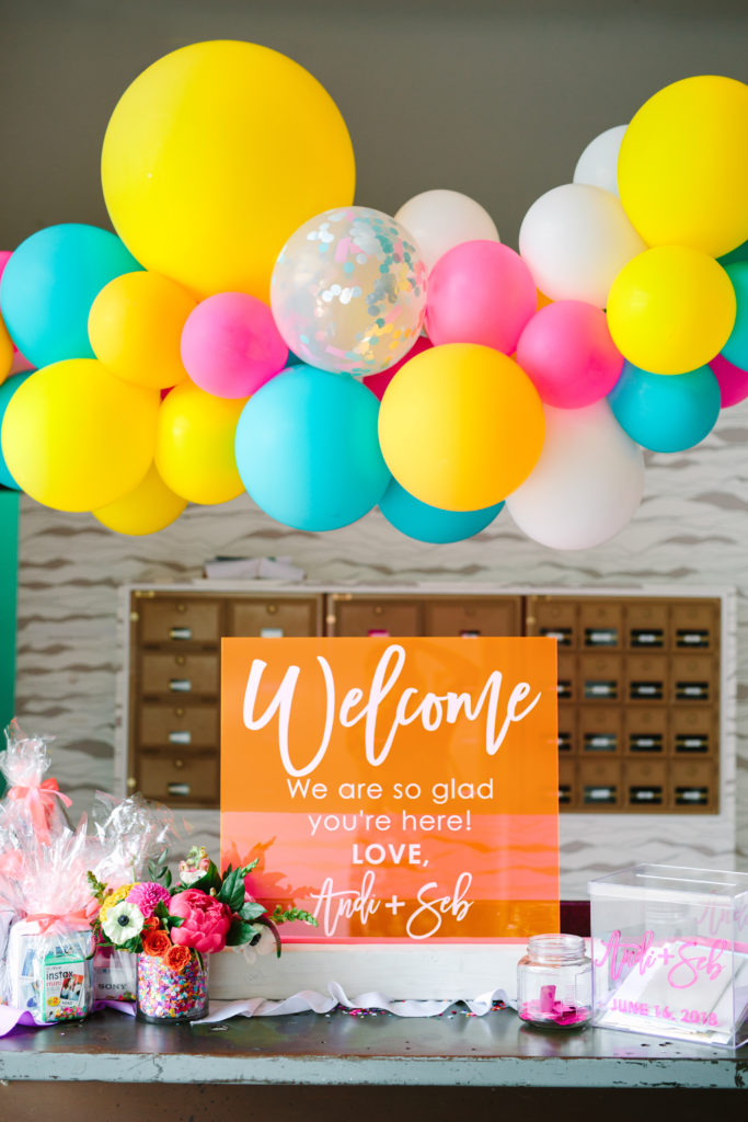A colorful wedding at Unique Space LA, welcome table with bright acrylic sign and balloon garland