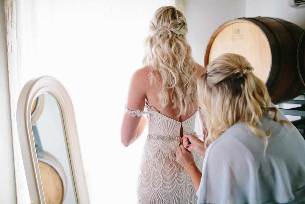 bride getting into her wedding dress with help of bridesmaid at Triunfo Creek Vineyards