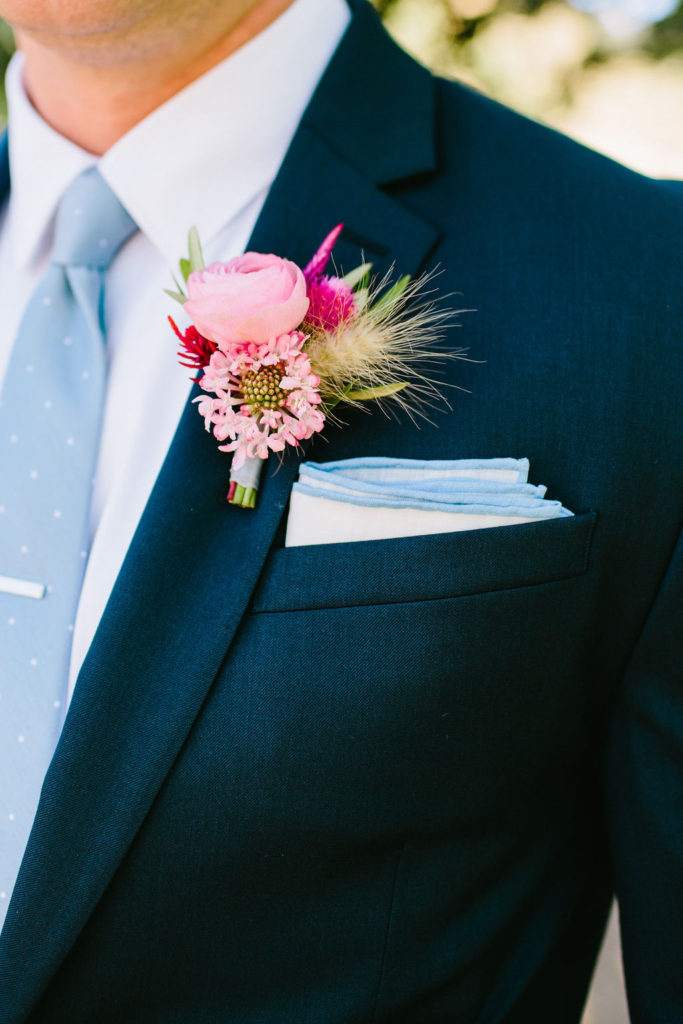 groom in dark navy suit and light blue tie with bright pink boutonniere at this bright vineyard wedding at Triunfo Creek Vineyards
