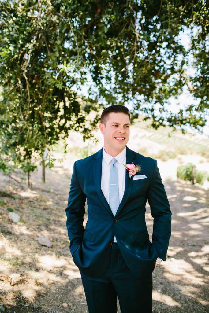 Groom portrait with dark navy suit, light blue tie and bright pink boutonniere at bright vineyard wedding at Triunfo Creek Vineyards