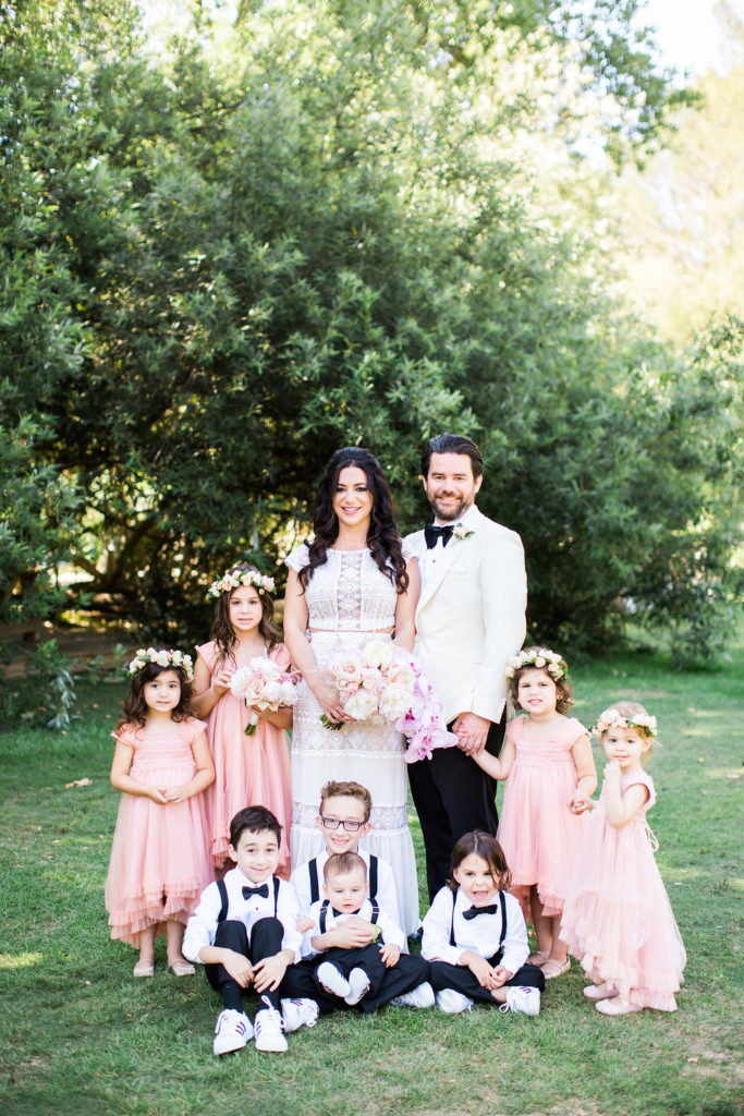 Bride and groom with flower girls in pink dresses and ring bearers in black suspenders for east coast meets west coast wedding at Calamigos Ranch