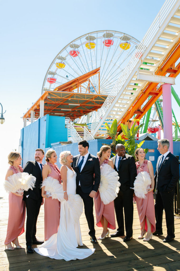 A glam and California infused wedding at Viceroy Santa Monica, wedding party photo at Santa Monica pier, bridesmaids in pink slip dresses and feathered fans, groomsmen in navy suits