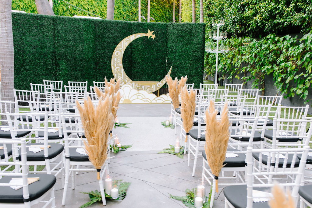A glam and California infused wedding ceremony at Viceroy Santa Monica with pampas grass, monstera leaves and gold moon backdrop
