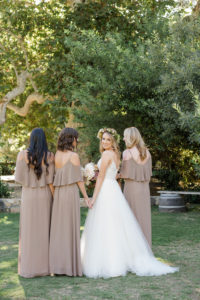 A chic rustic wedding at Calamigos Ranch, bridesmaids wearing taupe dresses, bride in spaghetti strap wedding dress wearing flower crown