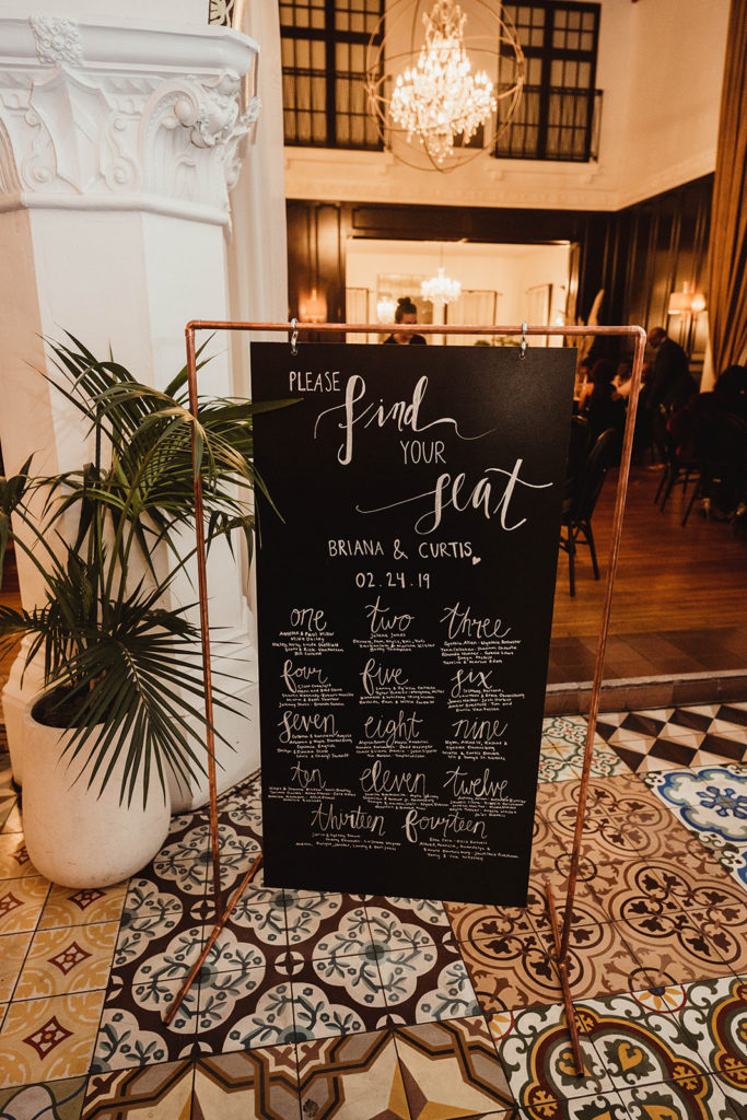 A romantic wedding reception at Ebell Long Beach, black seating chart with calligraphy