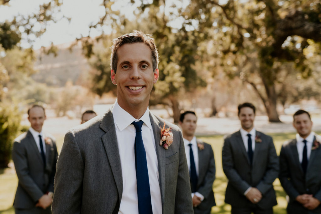 A whimsical wedding at Triunfo Creek Vineyards, groom in grey suit and navy blue tie with pink and orange boutonniere 