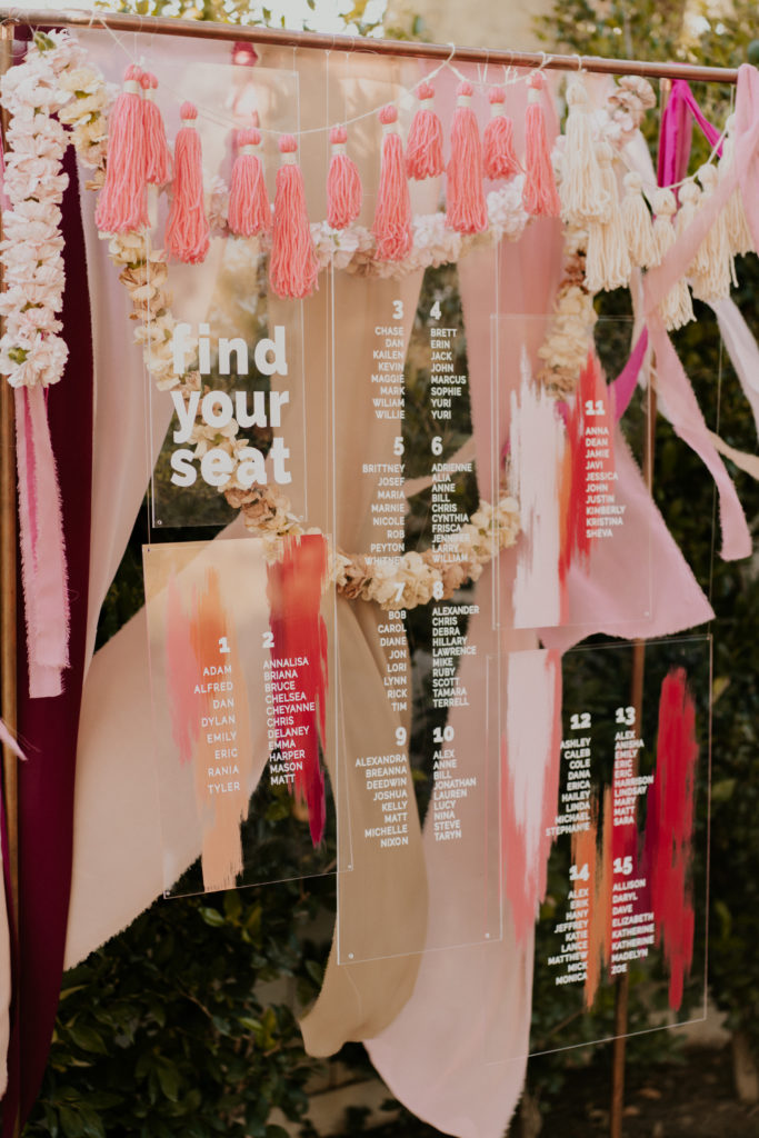A whimsical wedding reception at Triunfo Creek Vineyards, acrylic seating chart with pink tassels and garlands