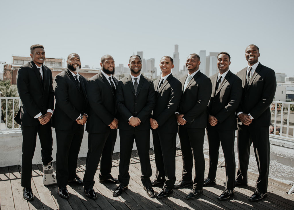 Beautiful wedding at The Unique Space in downtown LA, groomsmen in black suits with city skyline
