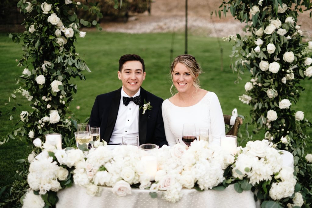 A Classic Vineyard Wedding reception at Triunfo Creek Vineyards, bride and groom at sweetheart table with green and white flowers
