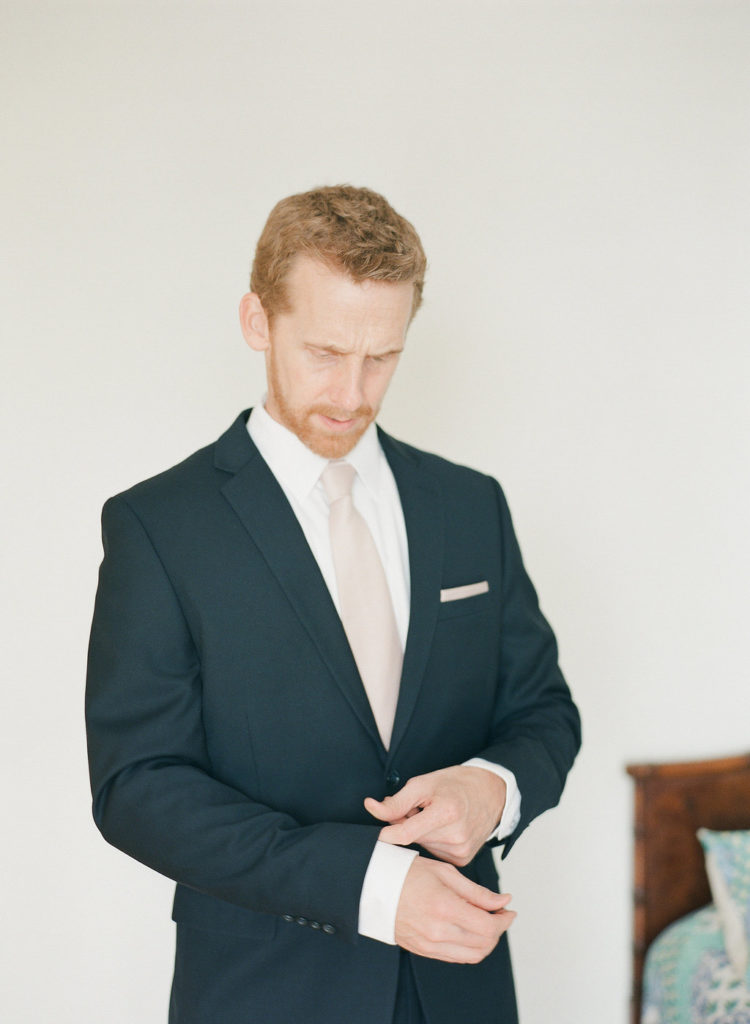 groom in black suit with pink tie getting ready for wedding day