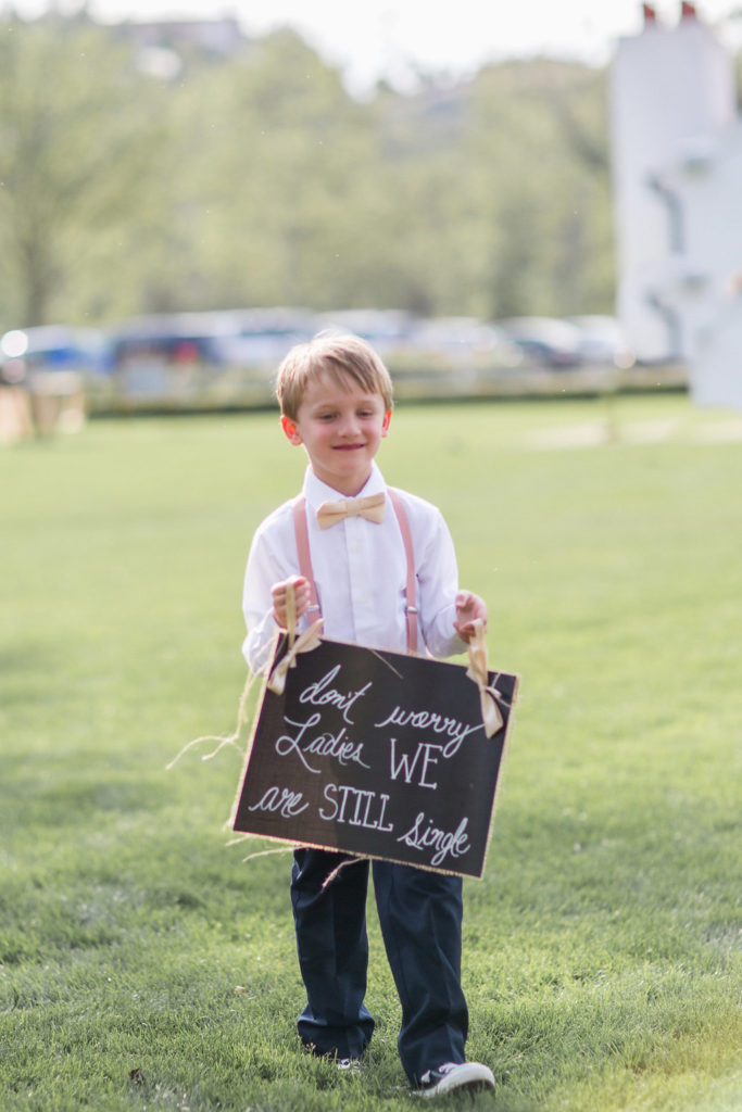 ring bearer with pink overalls holding chalkboard sign