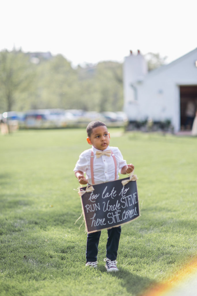 ring bearer with pink overalls holding chalkboard sign