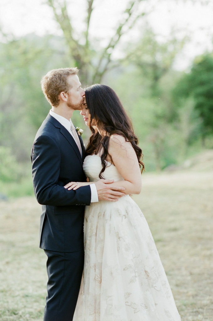 bride in strapless wedding dress with brocade details and groom with black suit and pink tie first look in vineyard
