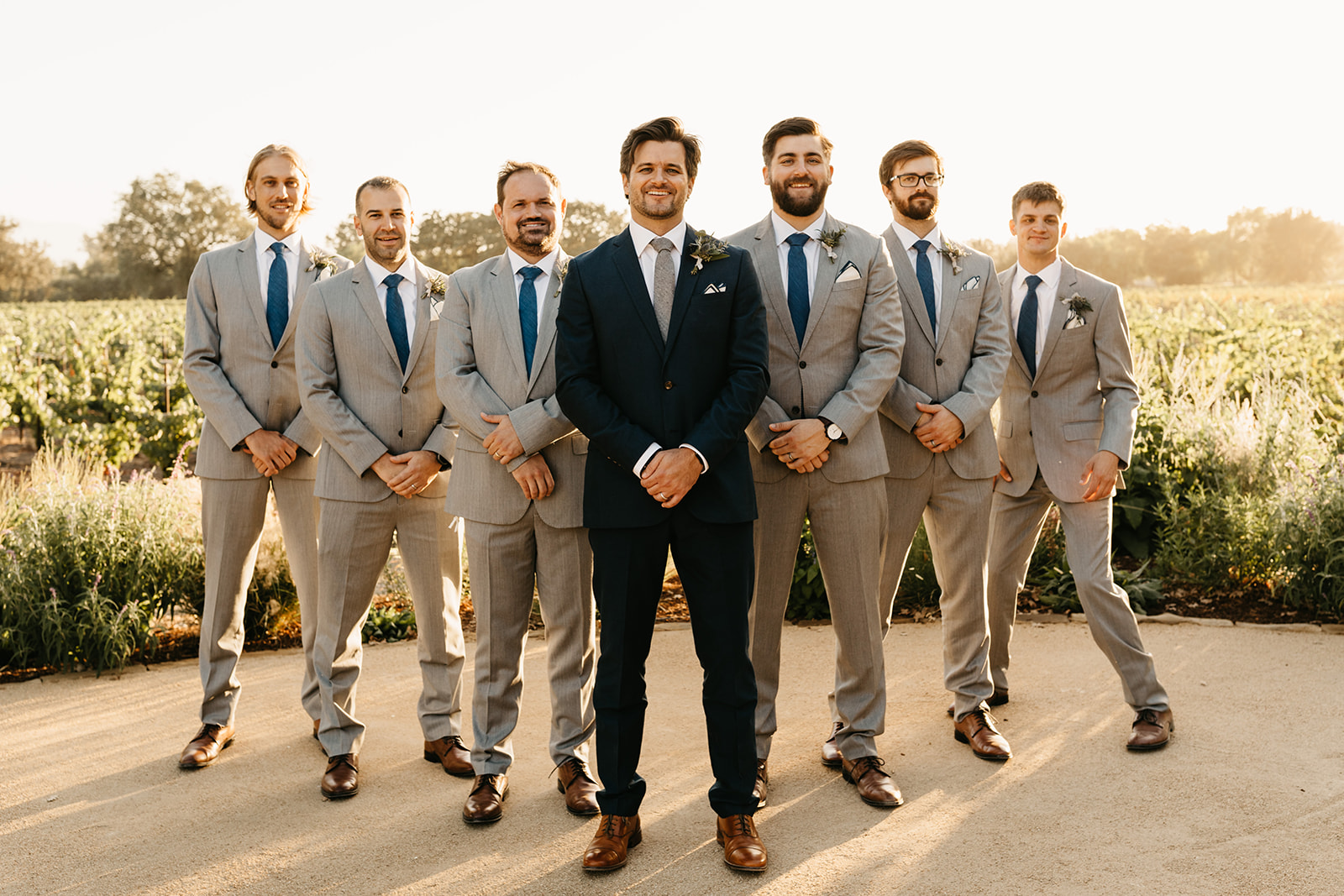 groom wearing dark blue suit with grey tie poses with groomsmen wearing grey suits with blue ties 