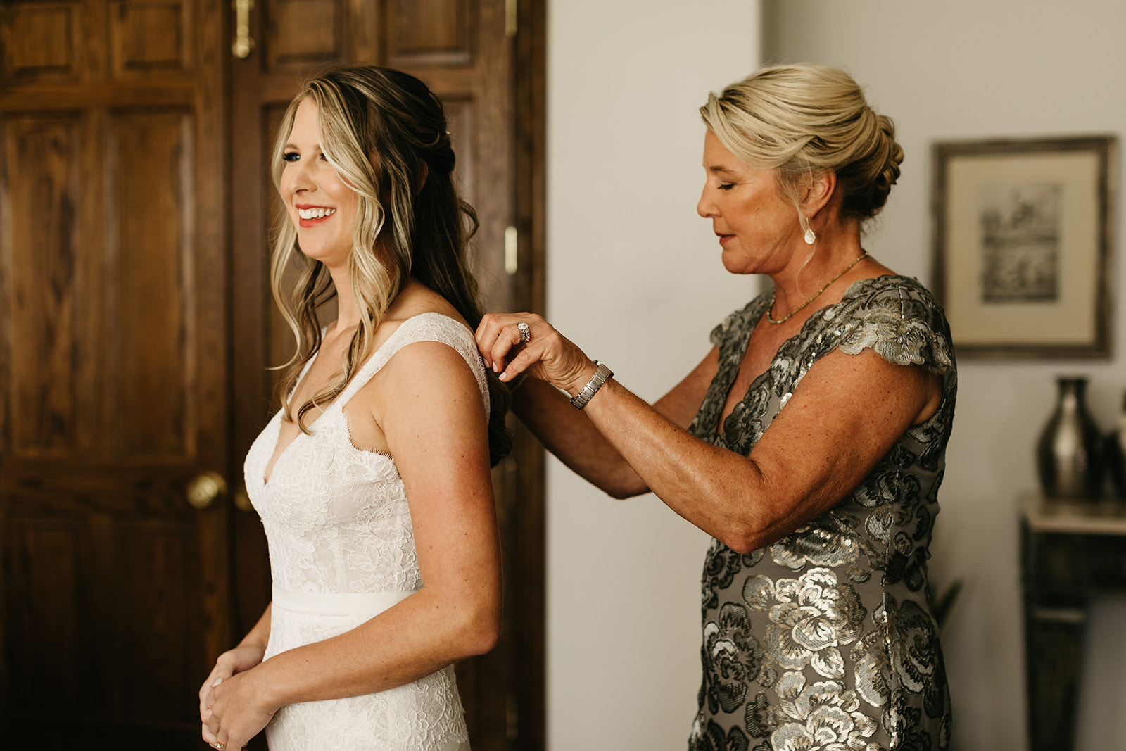 bride getting into her lace wedding dress with help of mom