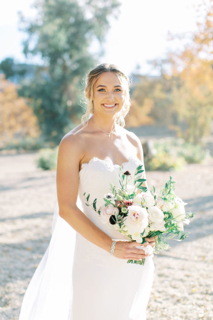 bride in lace wedding dress portrait shot in vineyard with green and white bridal bouquet