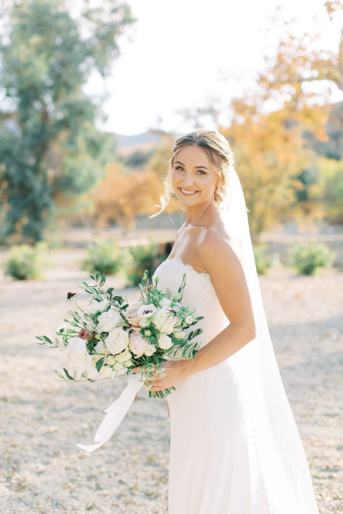 bride in lace wedding dress portrait shot in vineyard with green and white bridal bouquet