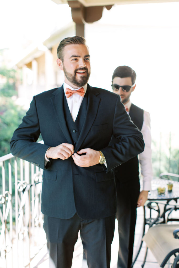 Groom in black suit with rust colored tie getting ready for wedding day