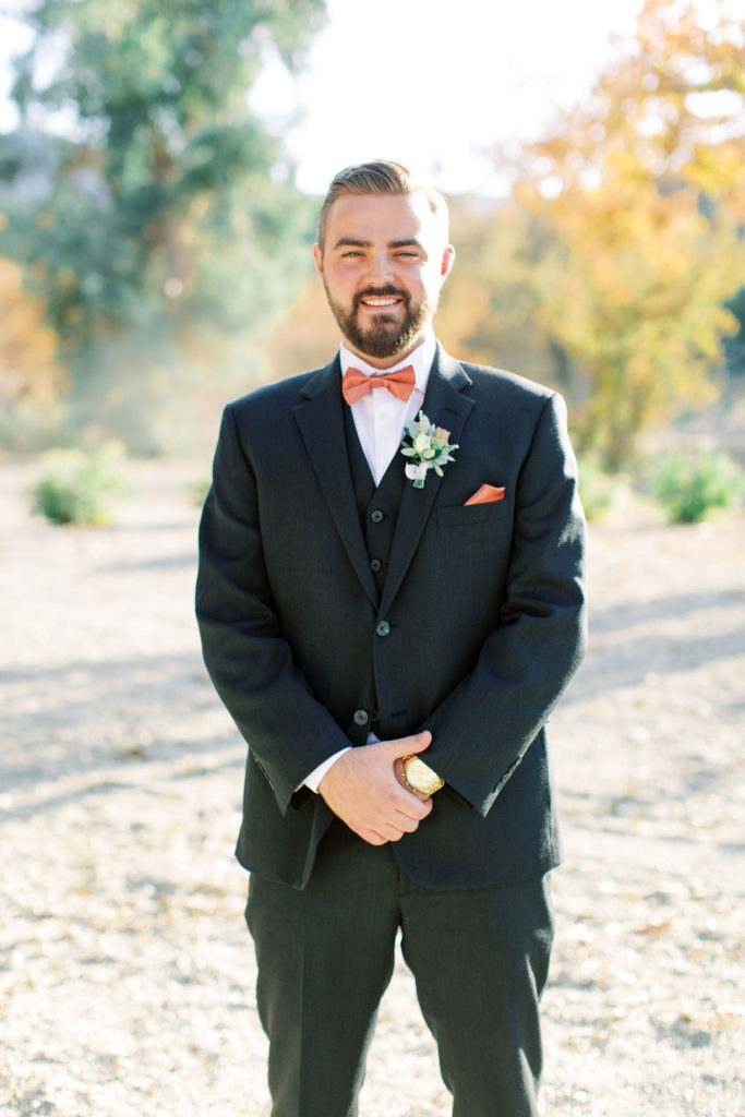 Groom in black suit with rust colored tie portrait shot in vineyard