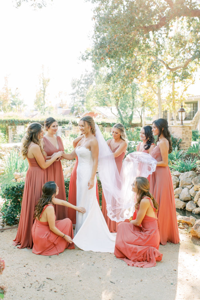 bride in lace wedding dress with bridesmaids in rust colored dresses getting ready for wedding day