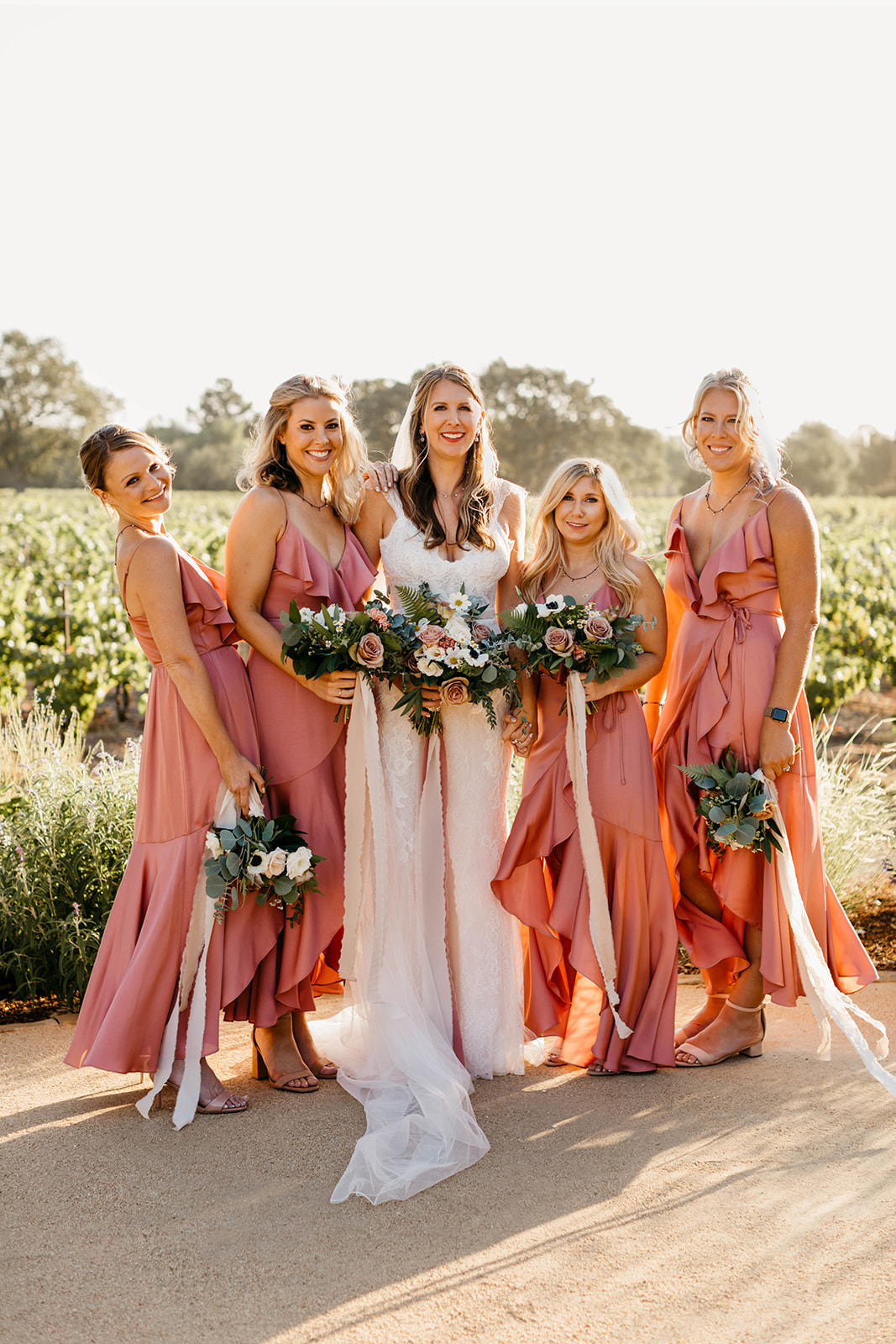 bride in lace wedding dress with bridesmaids in sunset pink satin dresses