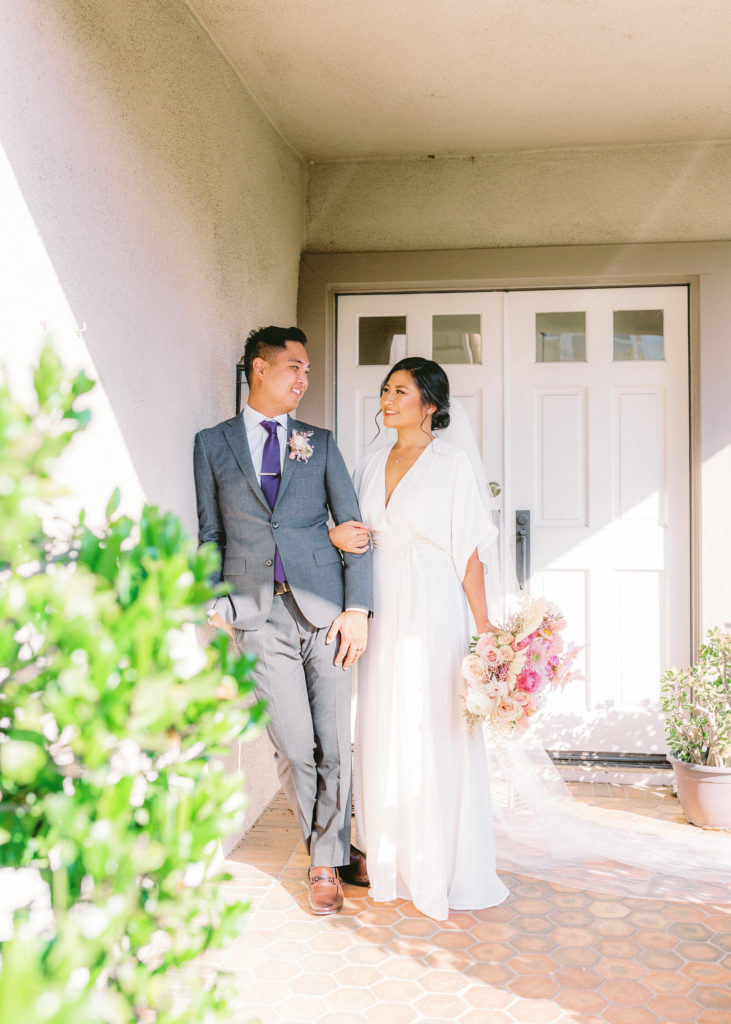 bride wearing Reformation wedding dress and groom with grey suit and purple tie portrait shot after wedding at home