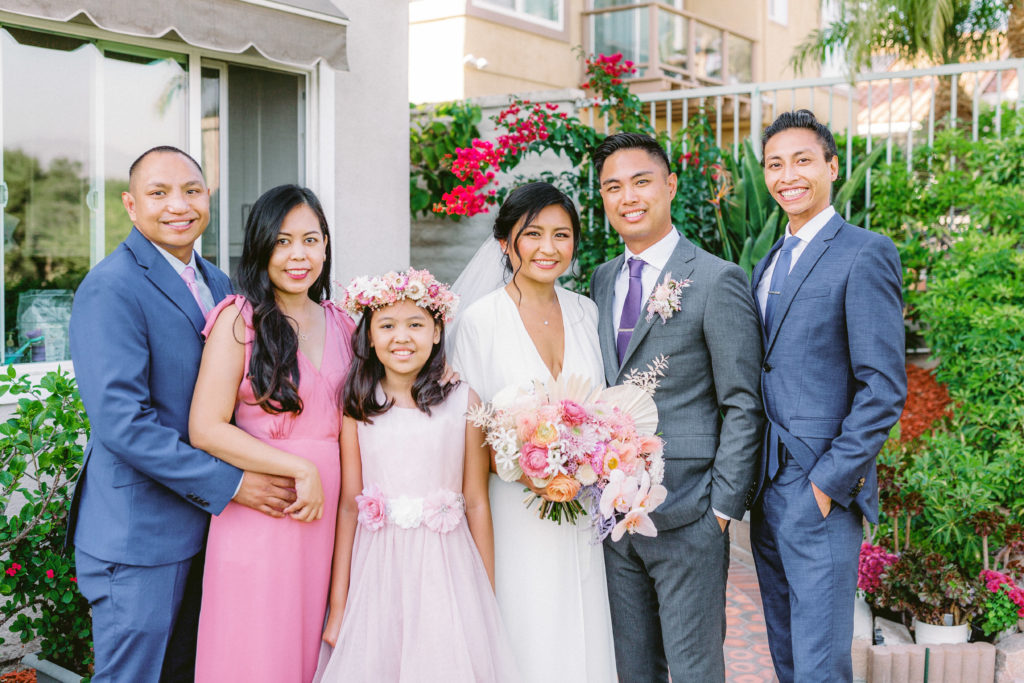 bride wearing Reformation wedding dress and groom with grey suit and purple tie portrait shot with family during small backyard ceremony