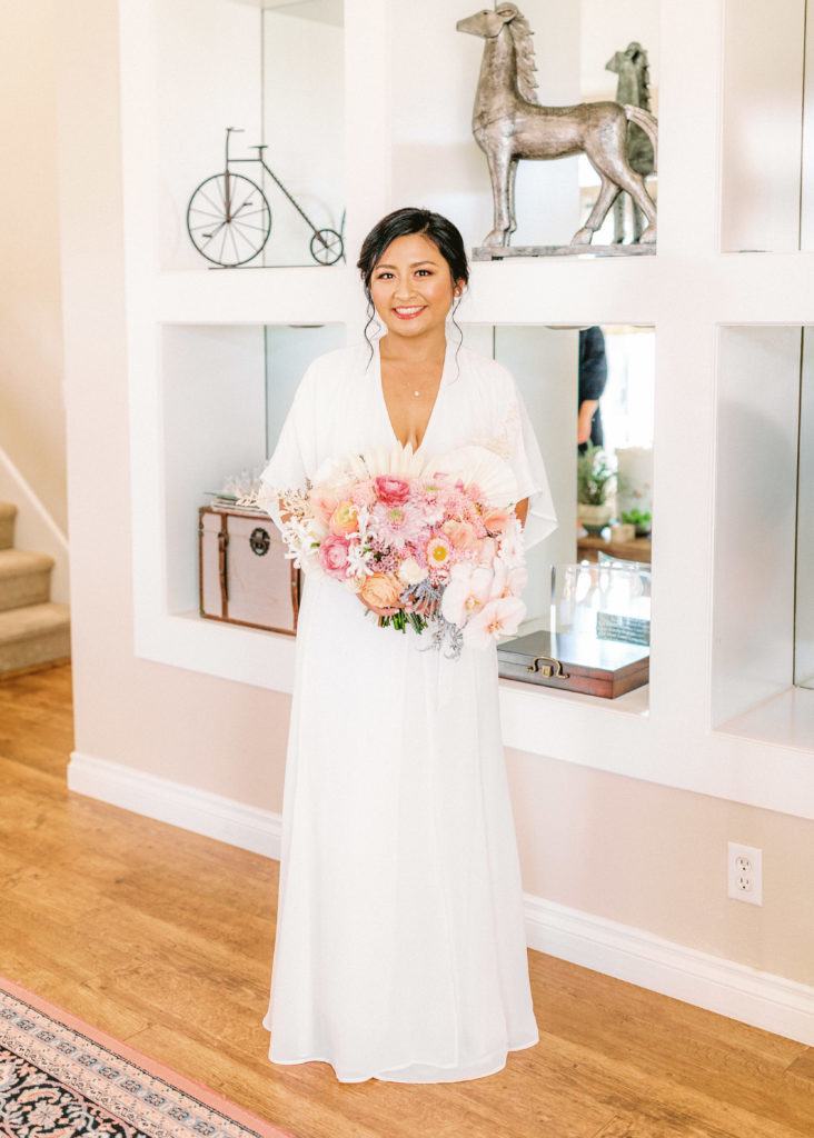 bride wearing Reformation wedding dress holding bouquet with pink and purple florals
