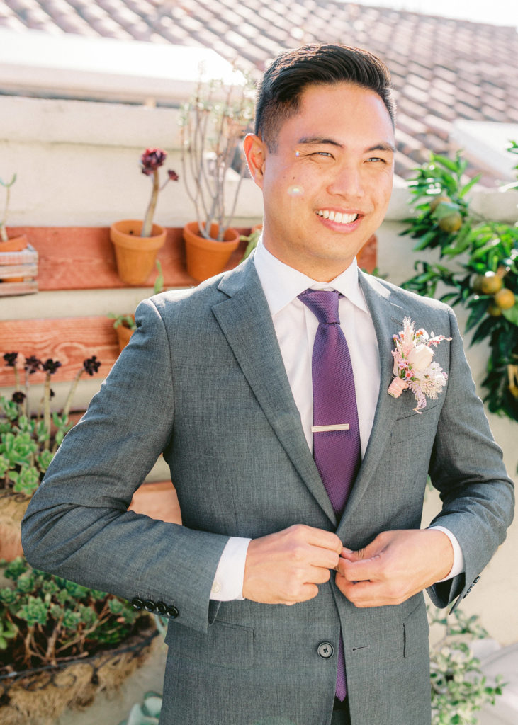 groom getting ready wearing light grey suit and purple tie with unique boutonniere 