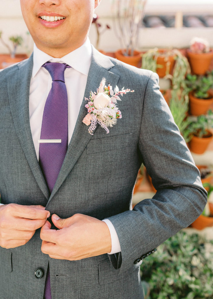 groom getting ready wearing light grey suit and purple tie with unique boutonniere 