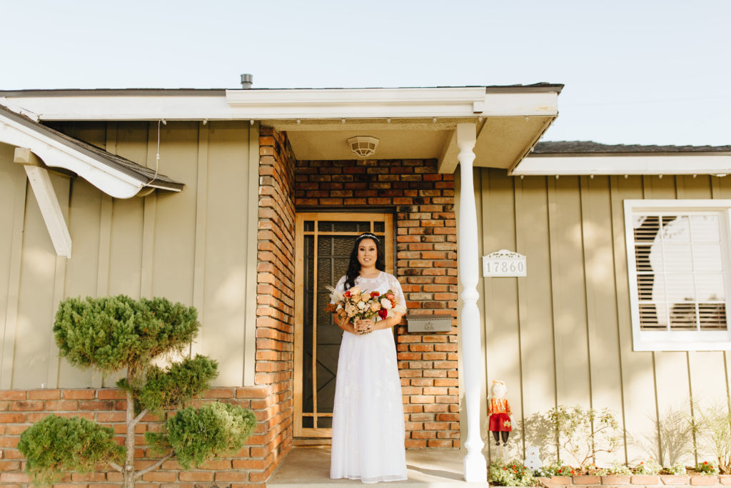 Bride in a bohemian style wedding dress with soft flutter sleeves and open back takes a portrait on her front porch before an intimate backyard wedding