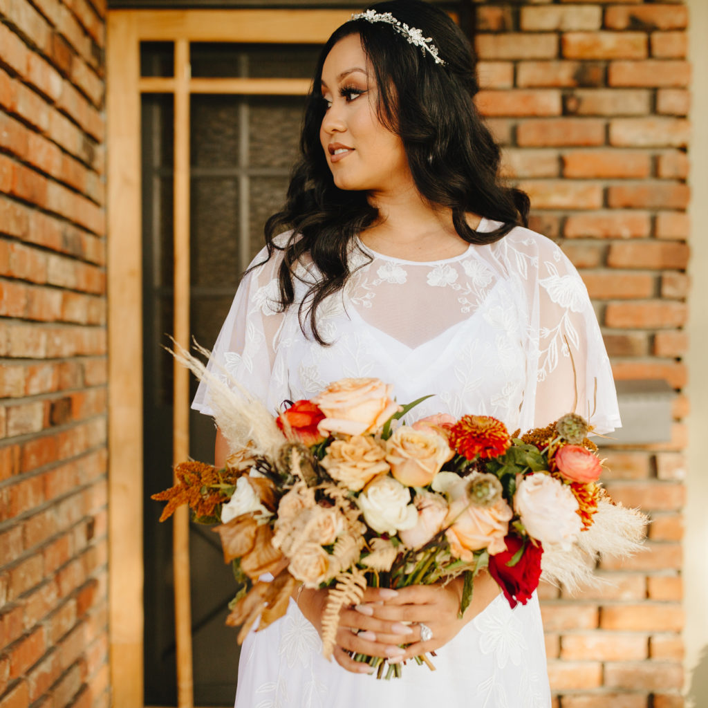 Bride in a bohemian style wedding dress with soft flutter sleeves and open back takes a portrait on her front porch before an intimate backyard wedding