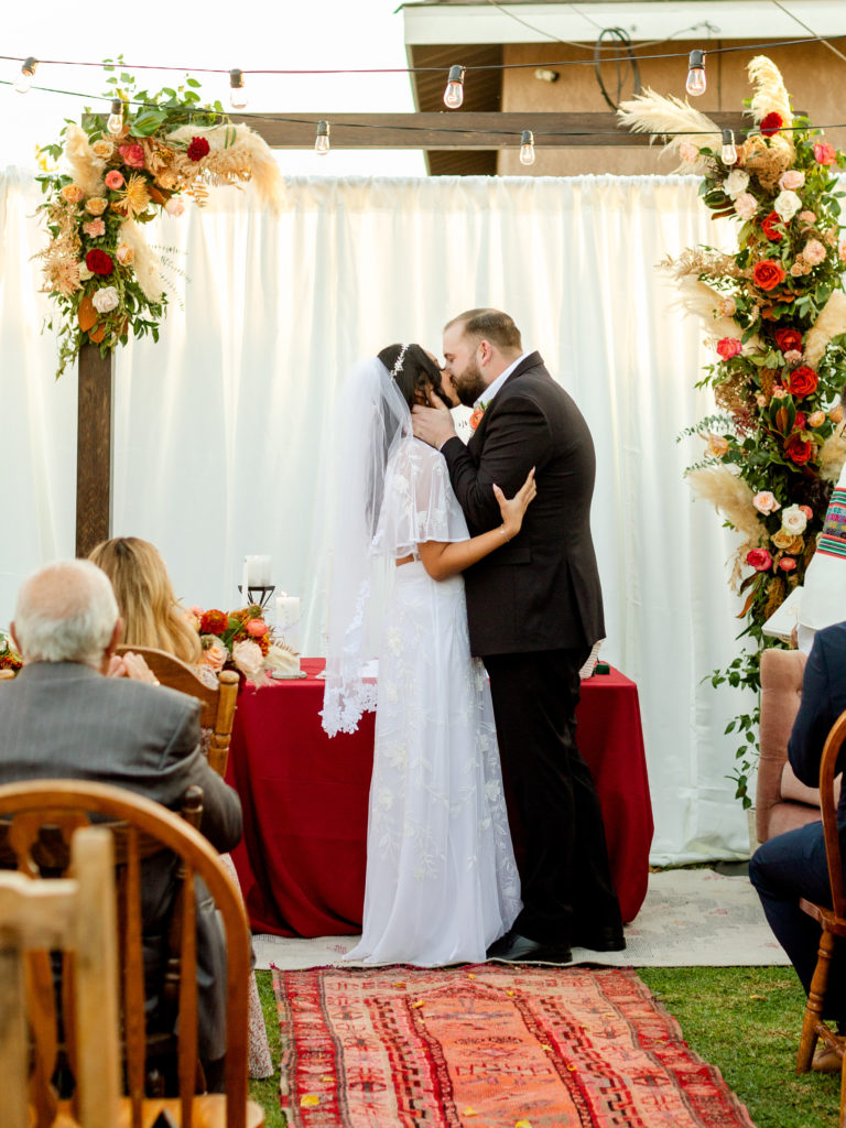 Bride and groom share a first kiss during Christian backyard wedding ceremony