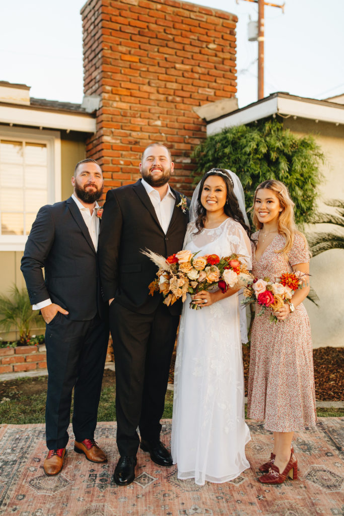 Bride and groom pose with groomsman and bridesmaid for small intimate backyard wedding