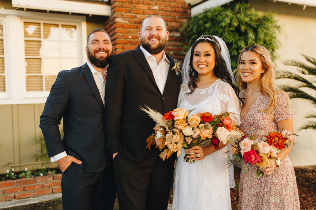 Bride and groom pose with groomsman and bridesmaid for small intimate backyard wedding