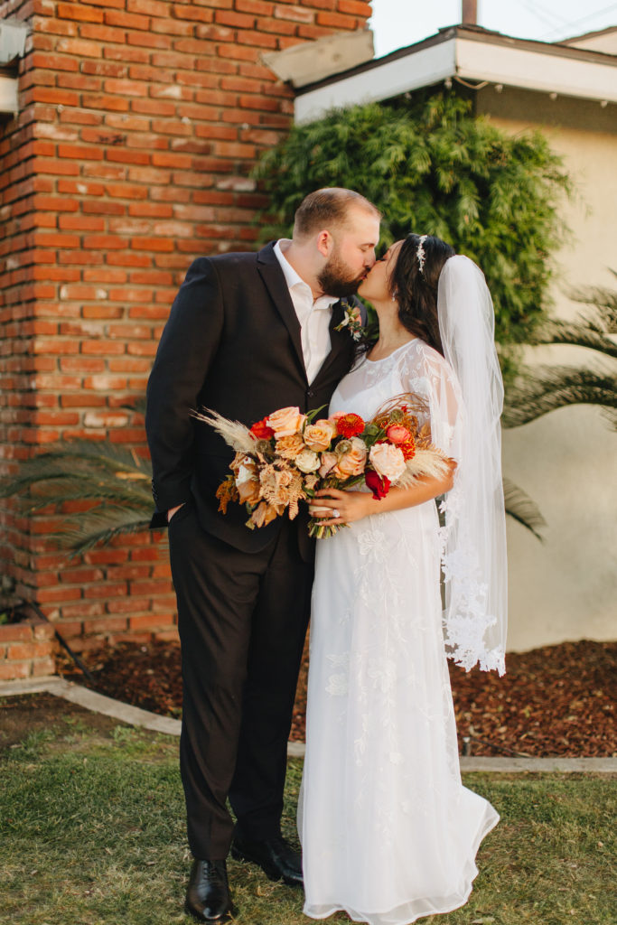Bride wearing bohemian style wedding dress and groom wearing black suit jacket portrait shot in front of their house after their backyard wedding ceremony