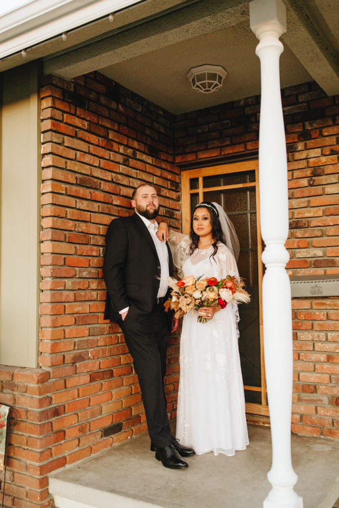 Bride wearing bohemian style wedding dress and groom wearing black suit jacket portrait shot in front of their house after their backyard wedding ceremony