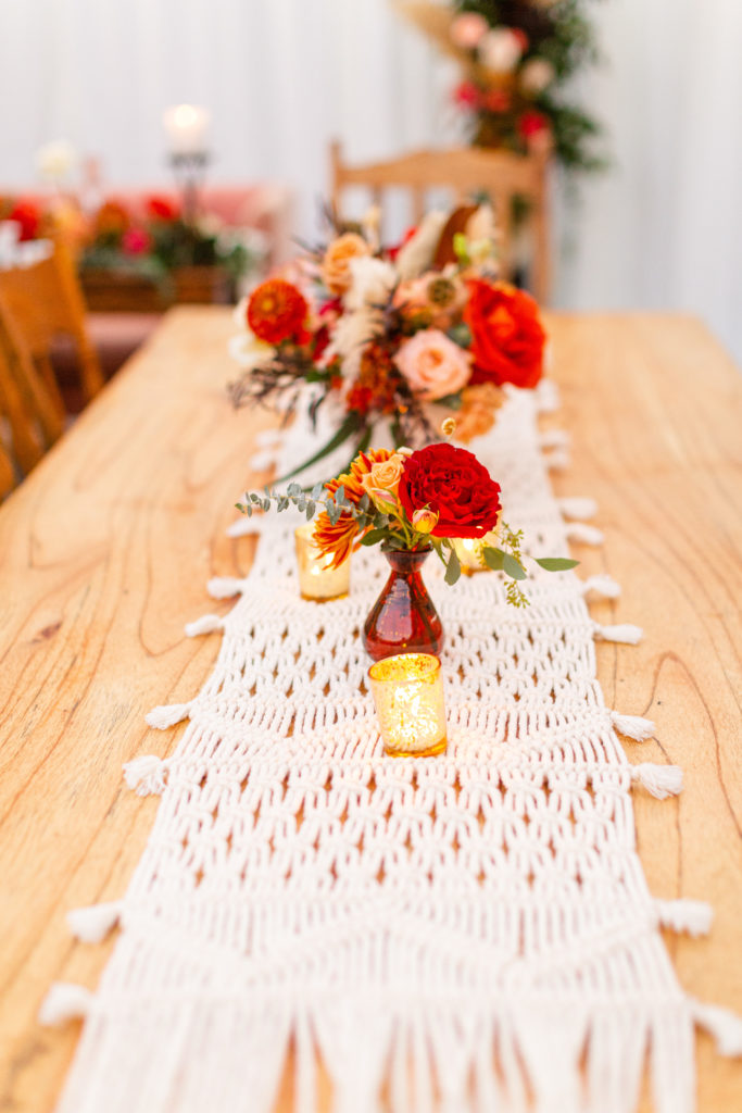 Bohemian style backyard wedding reception with macrame runners and bold red colors