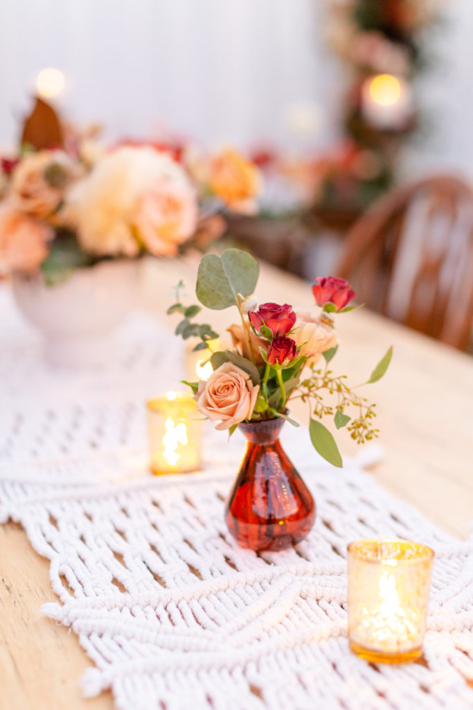 amber floral vase sits on a macrame runner in a Bohemian style backyard wedding reception