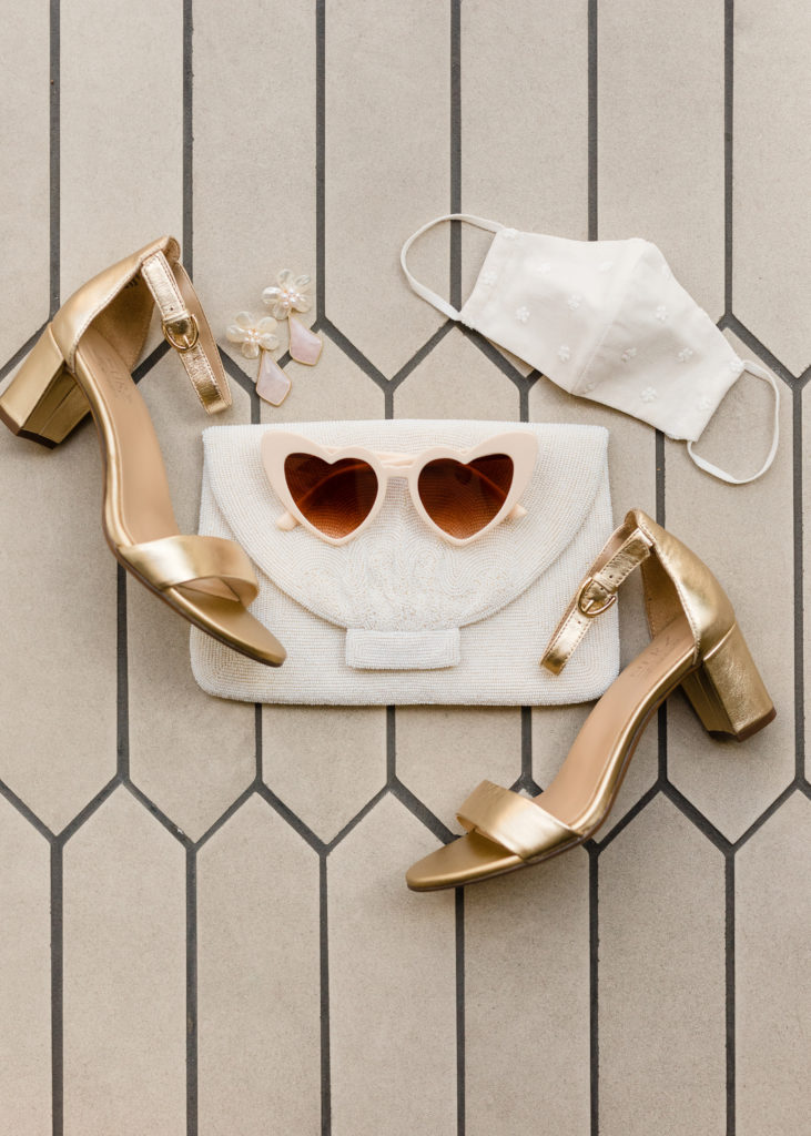 bridal accessories including gold shoes, lace face mask, beaded clutch and heart shaped sunglasses