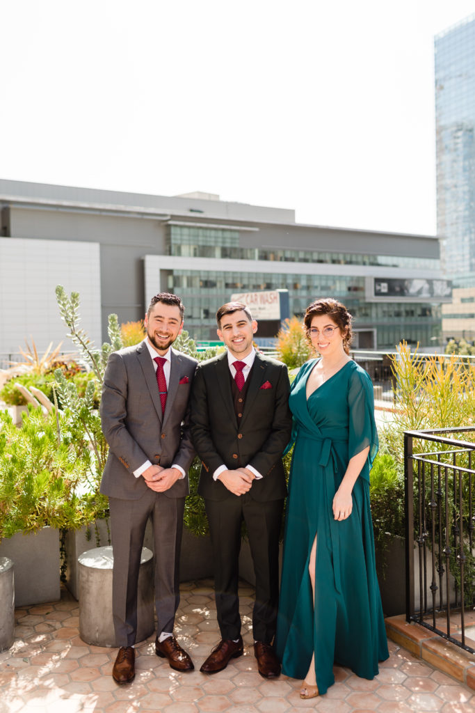 Groom wearing dark grey suit and red tie pose with brother and sister
