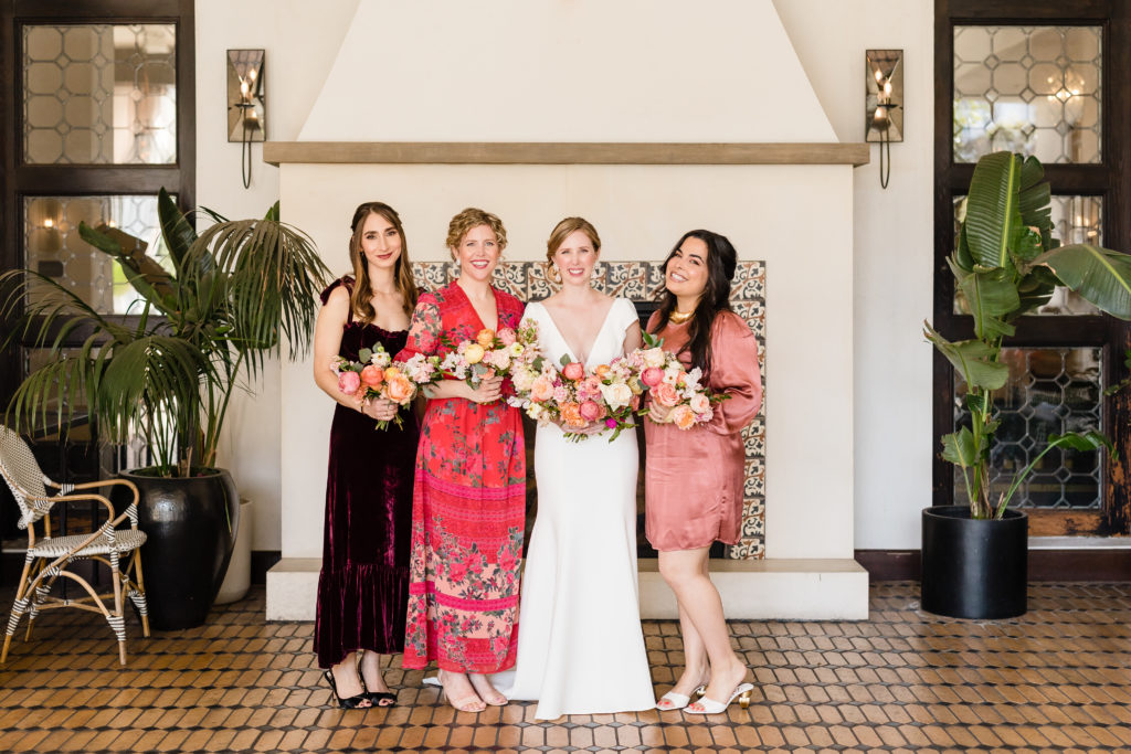 bride in deep v-neck wedding dress poses with bridesmaids in mix matched red dresses before spring wedding at Hotel Figueroa