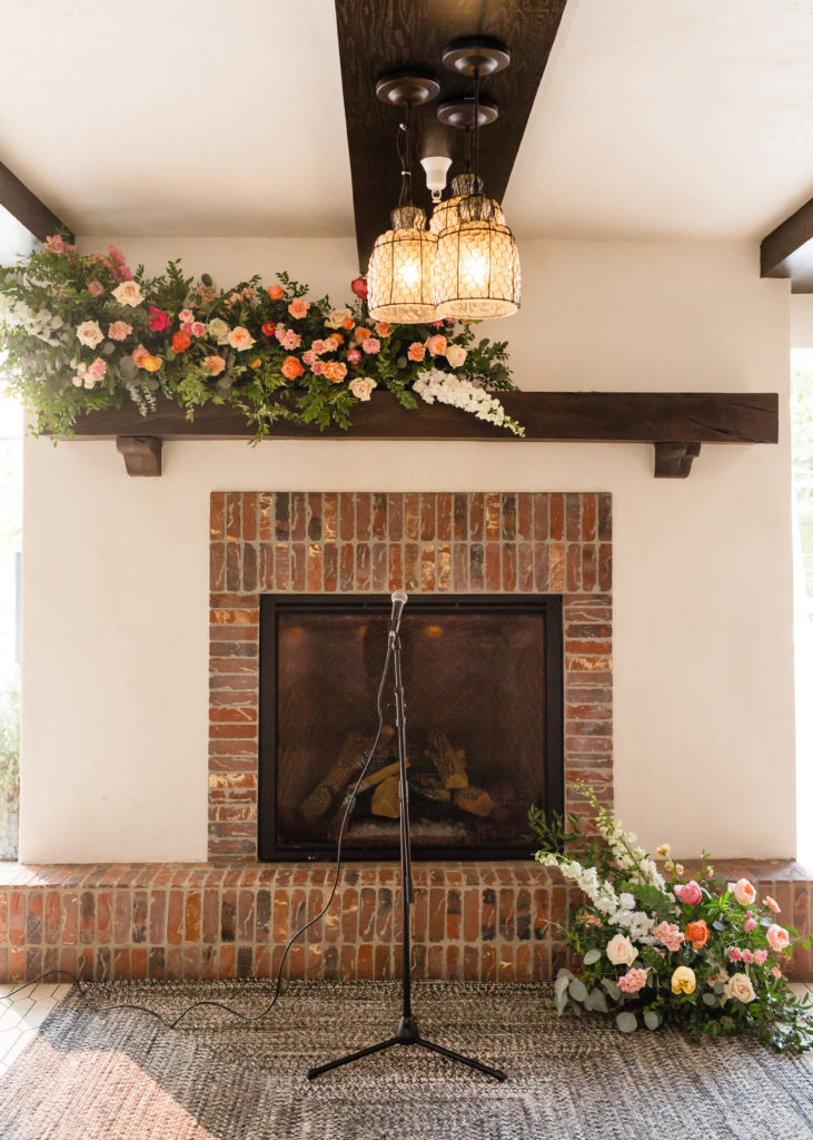Wedding ceremony at Ricks at Hotel Figueroa in front of fireplace with bright spring inspired floral arrangements  