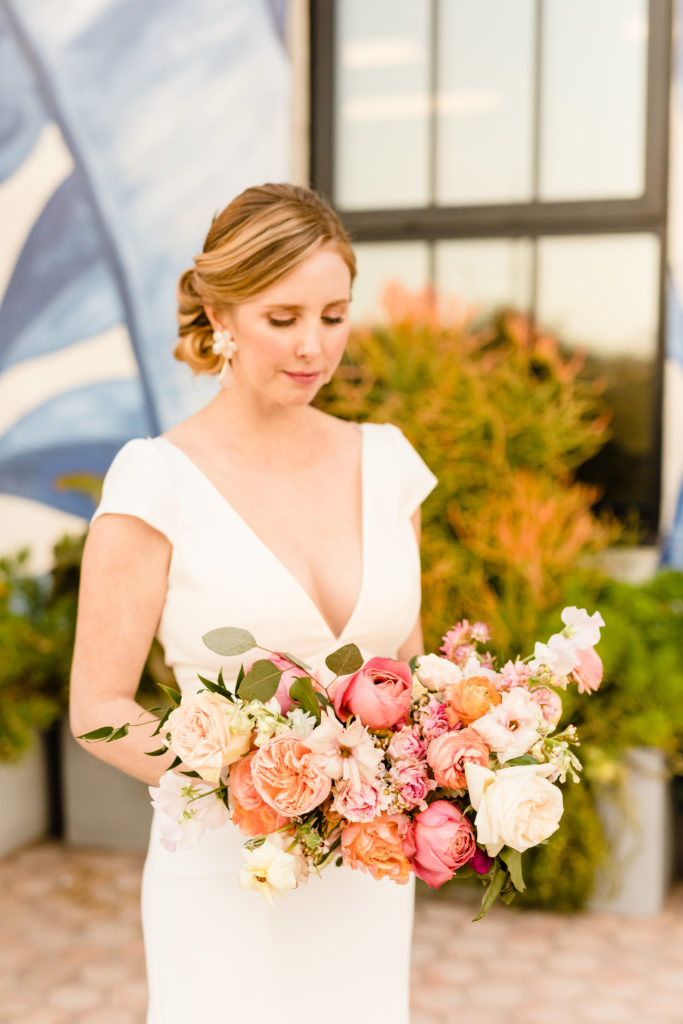 bride wearing deep v-neck wedding dress and low chignon bun holds bright spring inspired bridal bouquet 