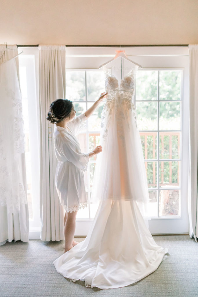 bride looking at wedding dress hanging in the window