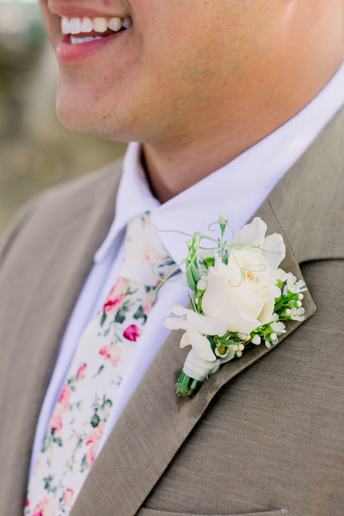 groom with tan suit, floral tie and white rose boutonniere