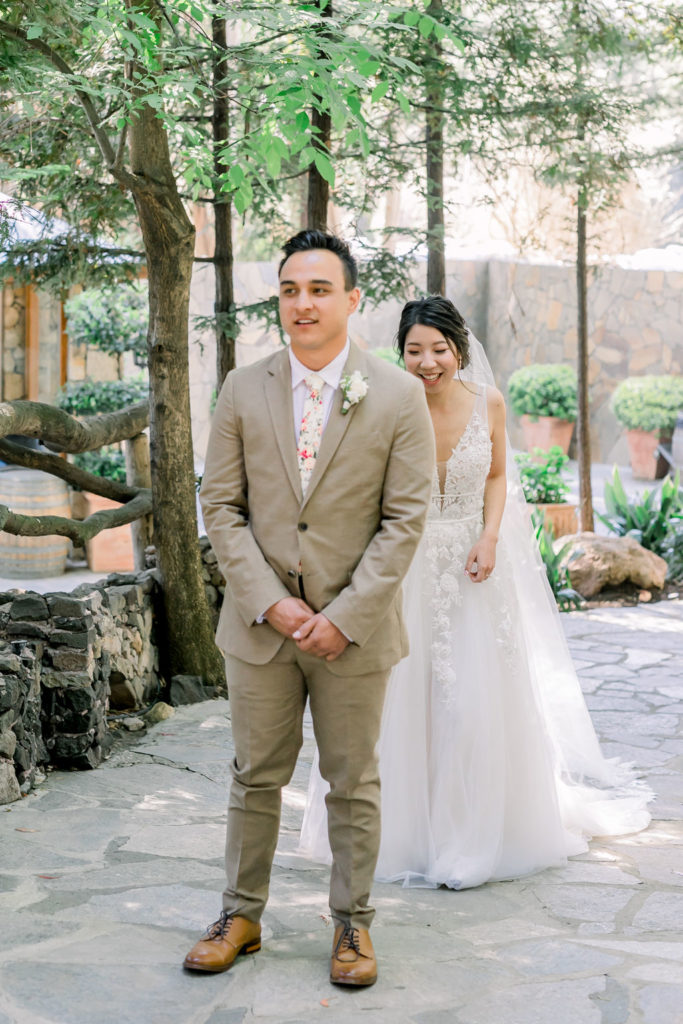 An enchanting wedding at Calamigos Ranch, groom in tan suit with floral tie has first look with bride wearing a floral lace appliqué deep v-neck wedding dress