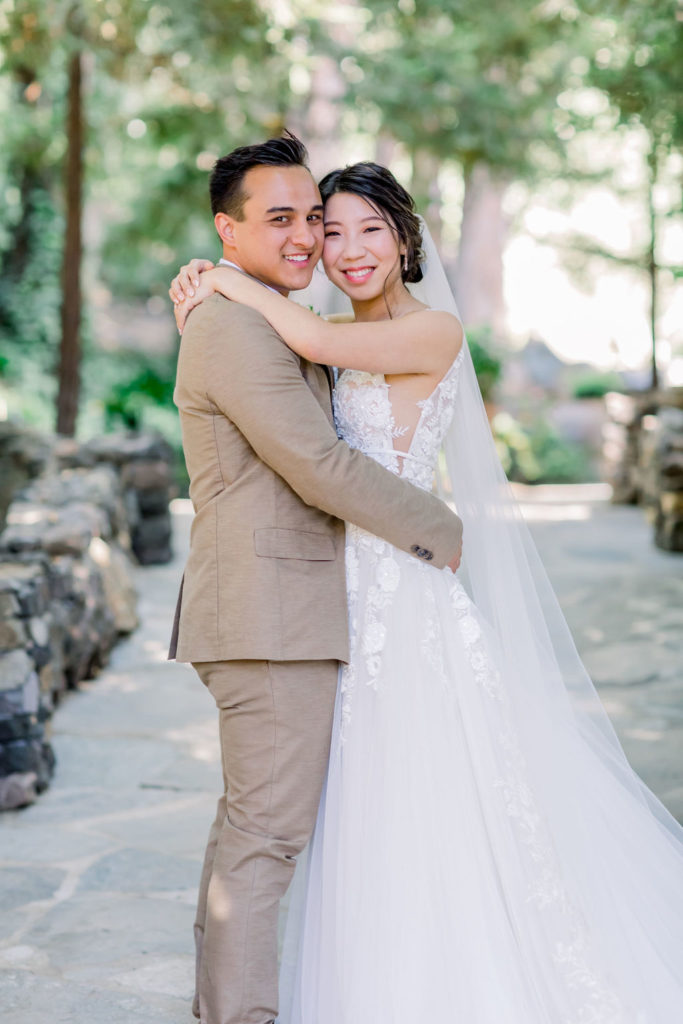 An enchanting wedding at Calamigos Ranch, groom in tan suit with floral tie has walks with bride wearing a floral lace appliqué deep v-neck wedding dress and cathedral length veil